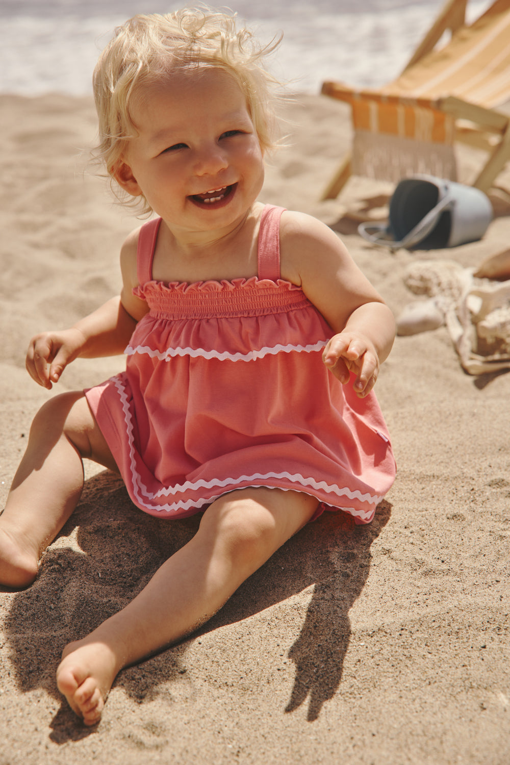 Baby sitting in the sand wearing the Beach Coral Smocked Top with Bloomer