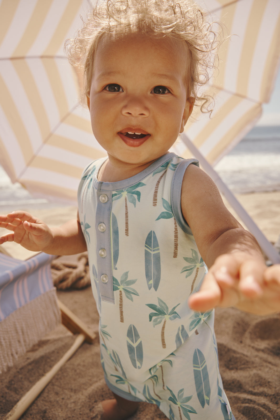 Baby wearing the Palm Dunes Tank Button Romper with an umbrella in the background