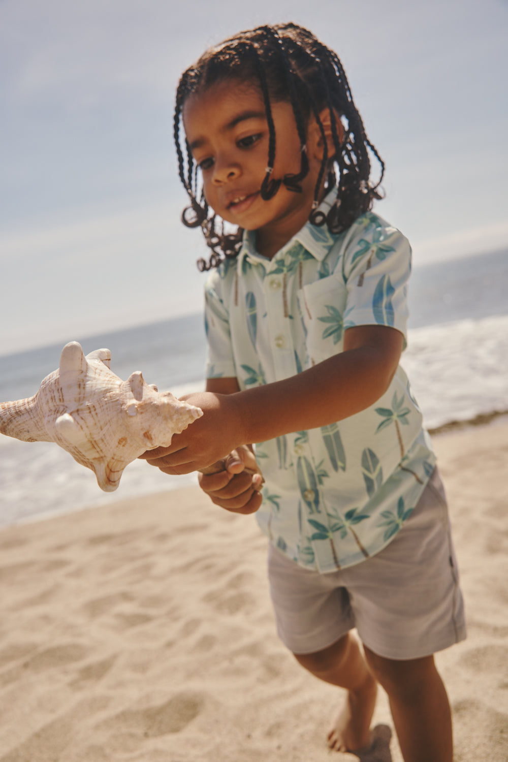Boy wearing the Palm Dunes Button Down Polo holding a shell