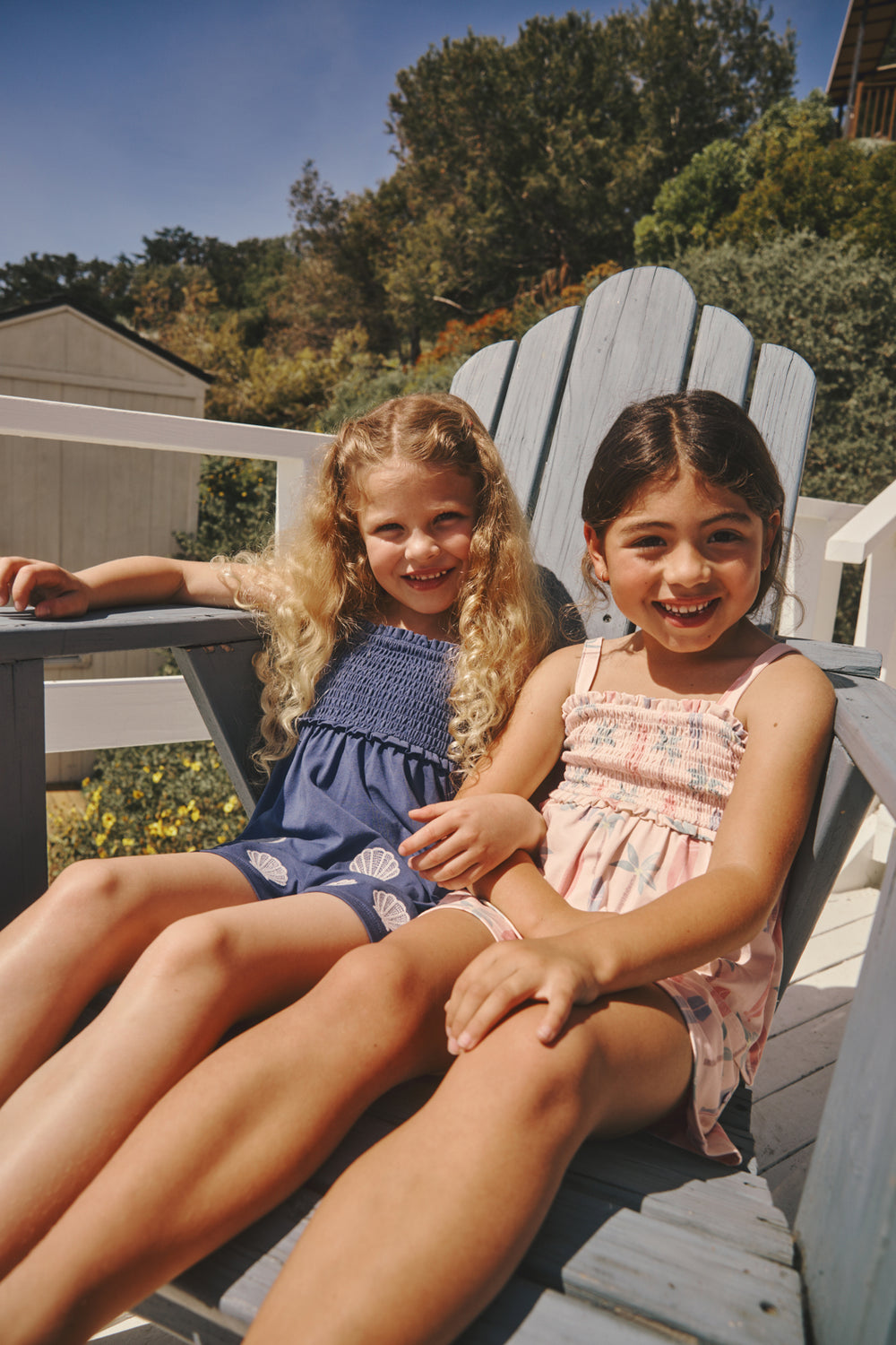 Two girls wearing Smocked Tank & Shorts Sets sitting on an adirondack chair 