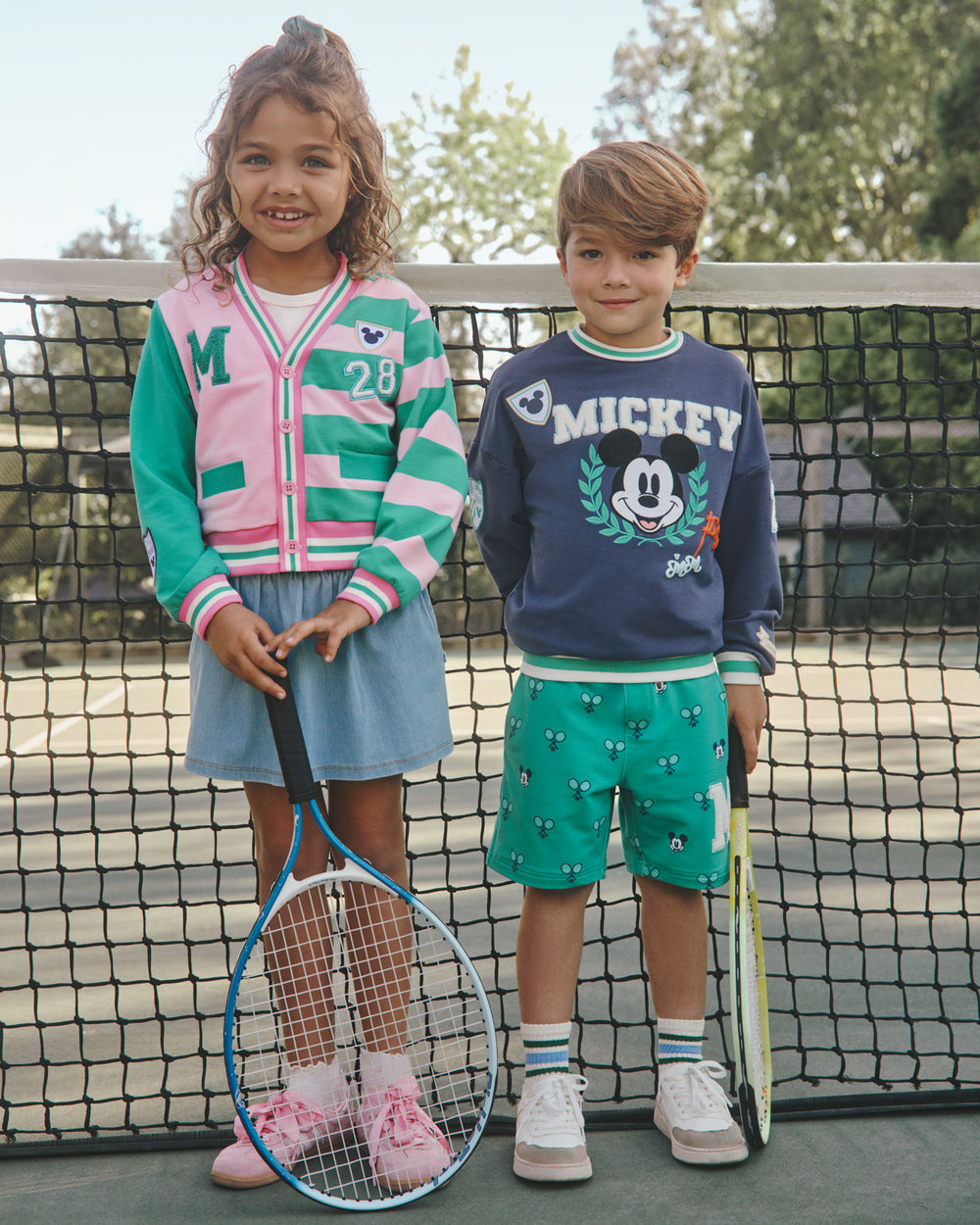Two children wearing Disney Mickey Mouse Sports Club Varsity styles on a tennis court