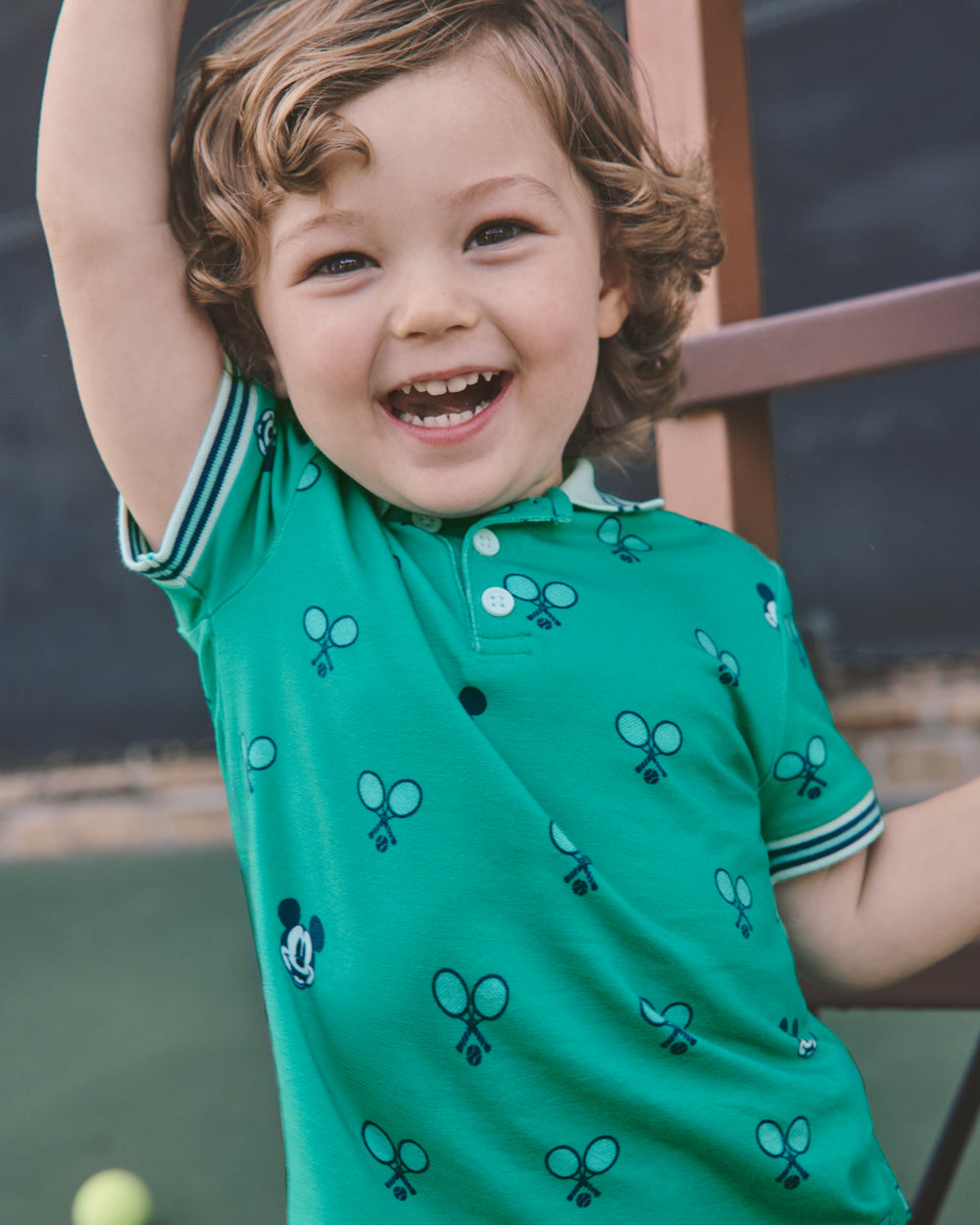 Close up of boy wearing the Disney Mickey Mouse Racket Rally Polo Shirt on a tennis court