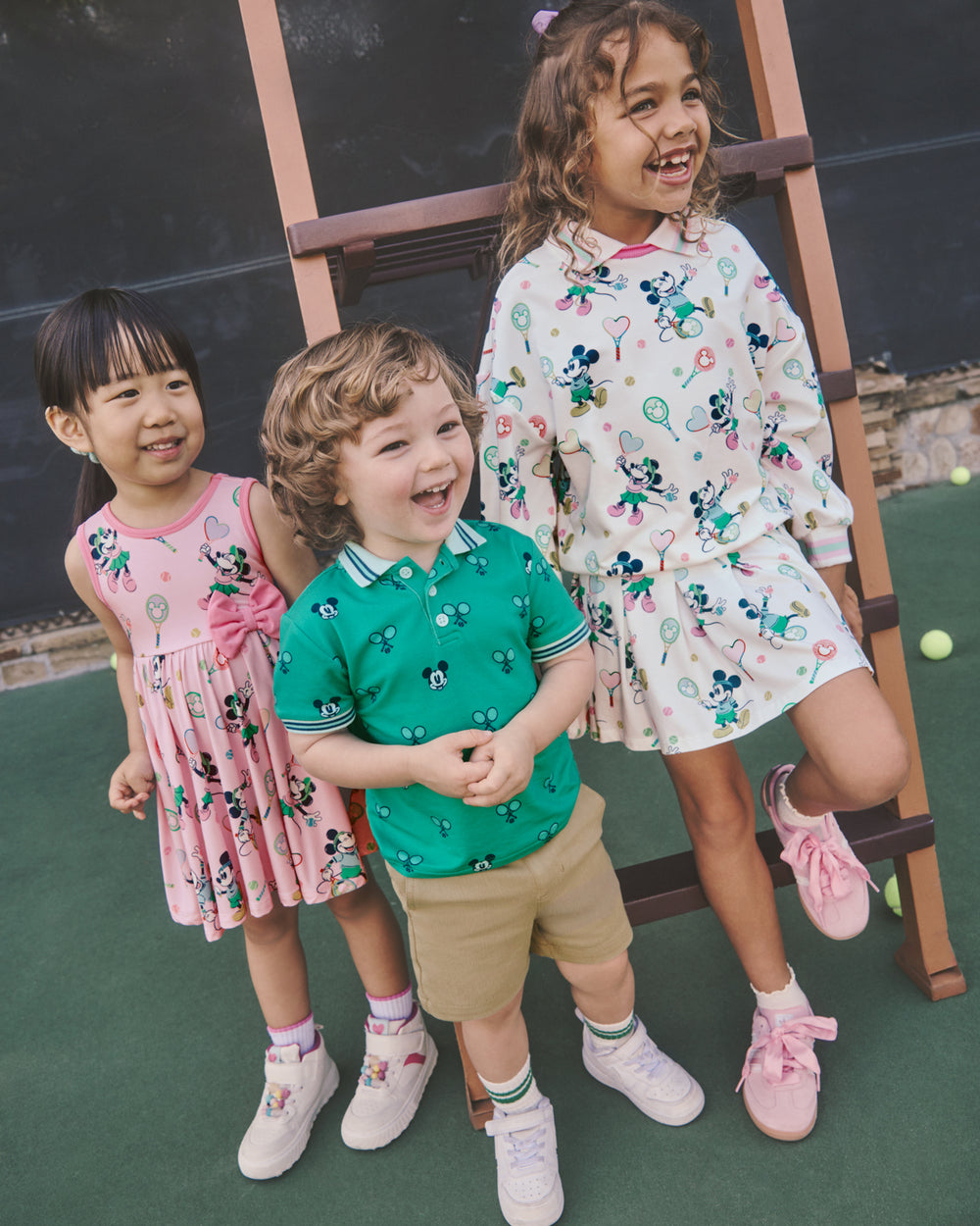 Three children wearing Disney Mickey Mouse Varsity Play styles on a tennis court