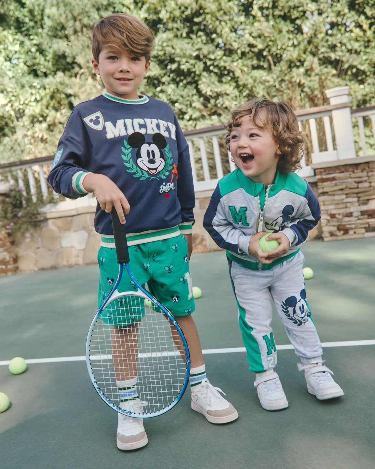 Two boys wearing Disney Mickey Mouse Sports Club Varsity styles on a tennis court