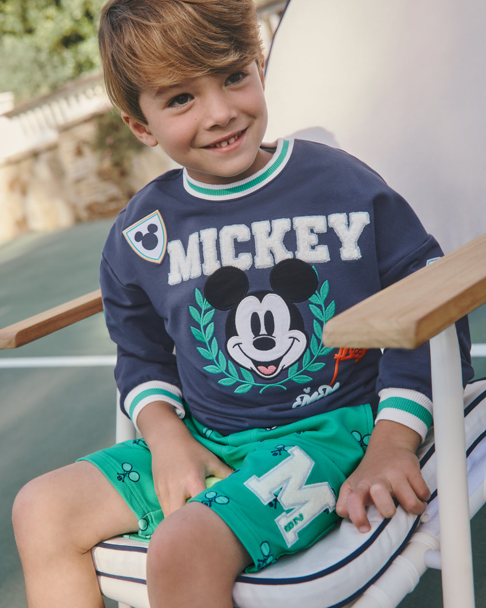 Boy wearing the Disney Mickey Mouse Sports Club Drop Shoulder Crewneck sitting in a lounge chair