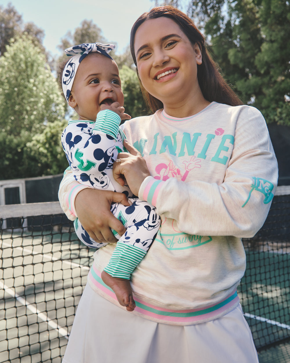 Mother wearing the Disney Minnie Mouse Queen of Swing Women's Crewneck Sweatshirt holding baby wearing the Disney Varsity Mickey Mouse Zippy