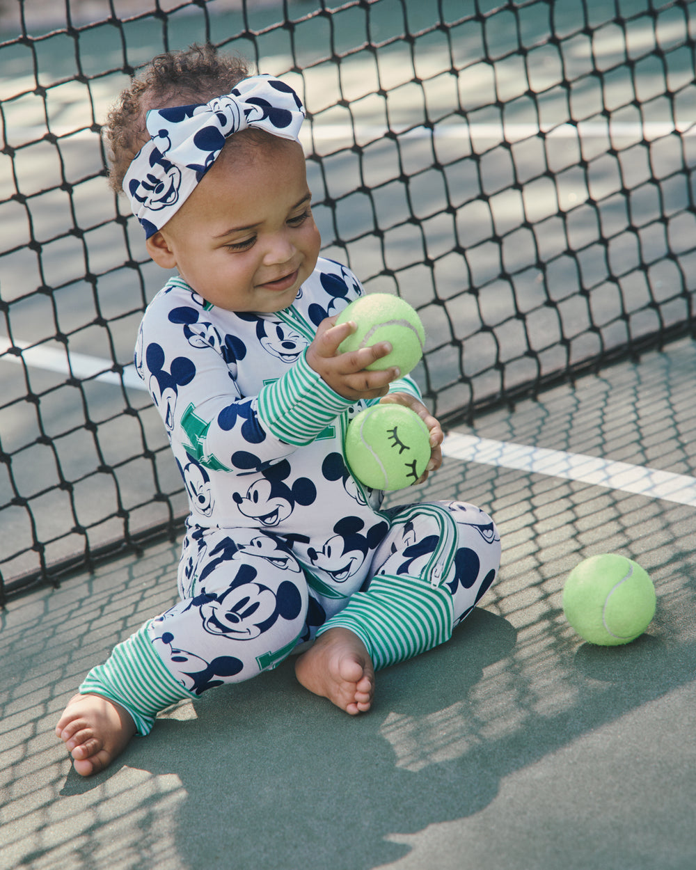 Baby wearing the Disney Varsity Mickey Mouse Zippy playing with tennis balls