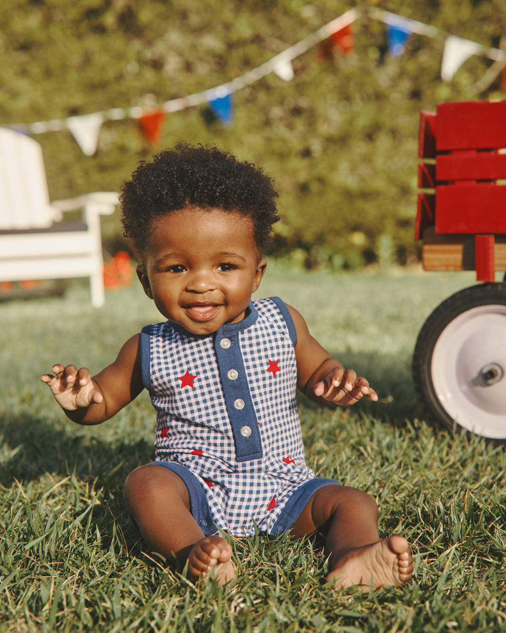 Boy wearing the Blue Ribbon Gingham Henley Romper sitting in the grass