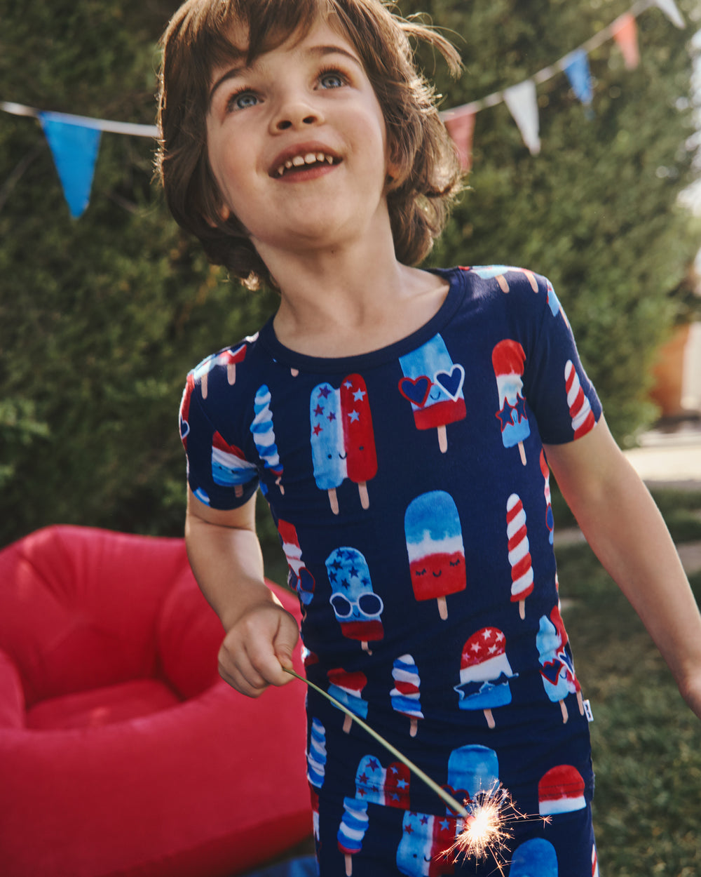 Boy holding a sparkler wearing the Sparkle Treats Two-Piece Short Sleeve & Shorts Pajama Set