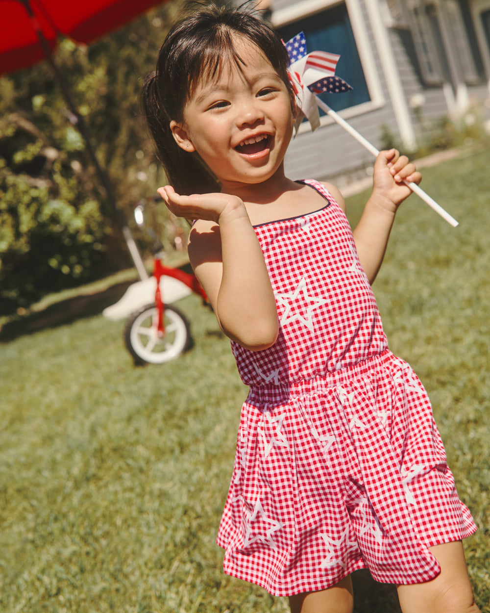 Girl wearing the Celebration Gingham Bow Back Twirl Dress with a 4th of July pinwheel