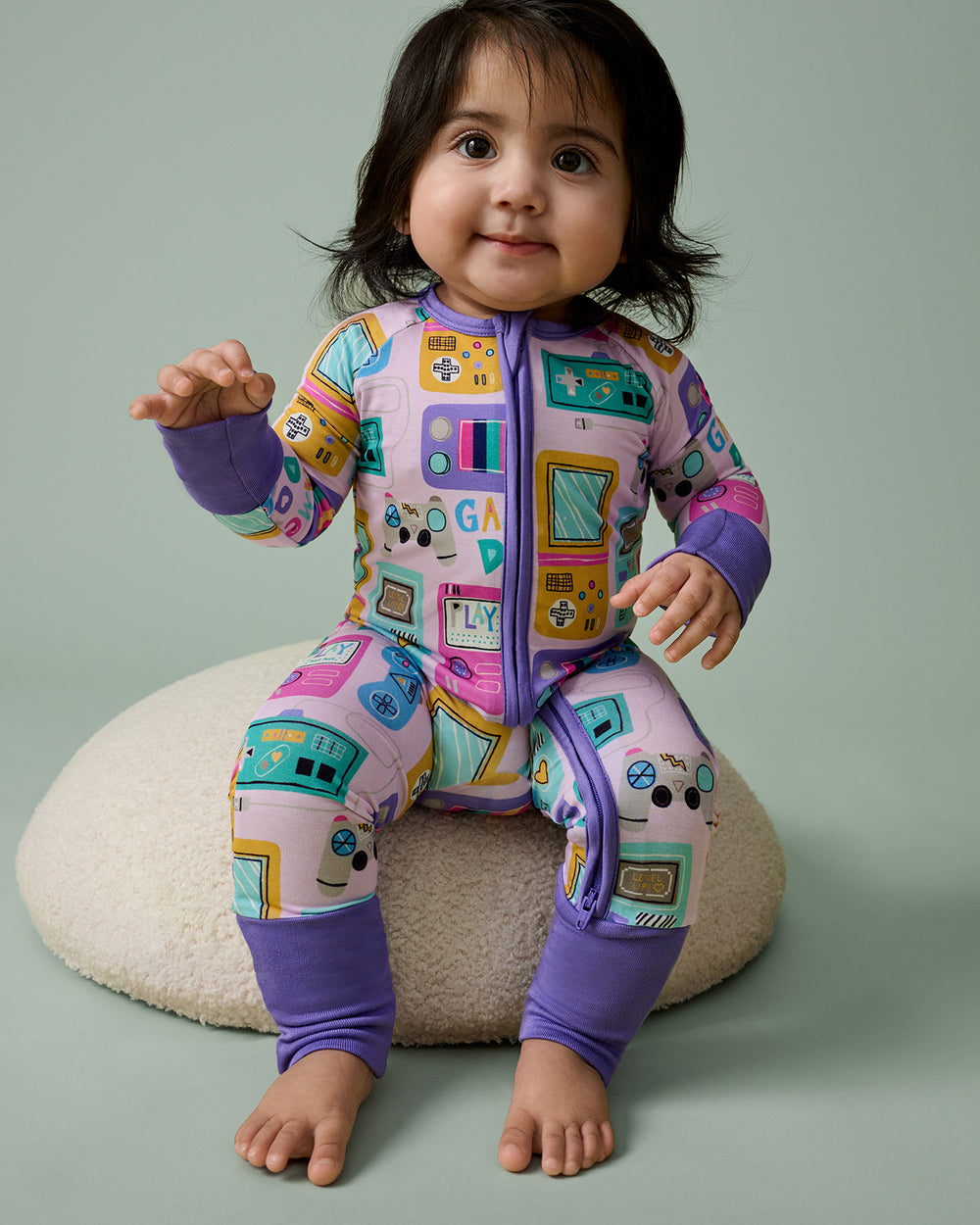 Baby sitting on a boucle ottoman wearing the Purple Game On Zippy
