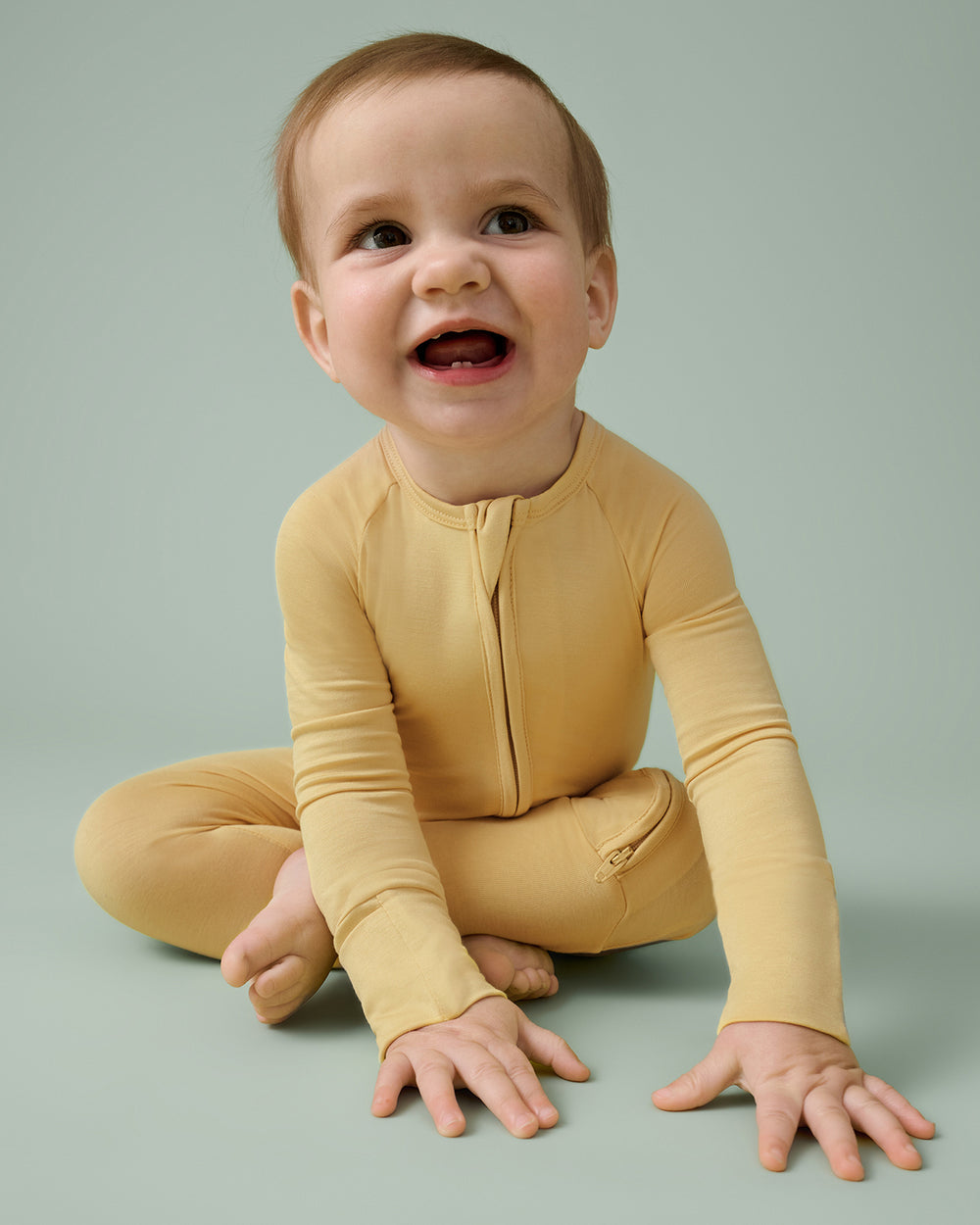 Baby wearing the Sunglow Zippy on a green backdrop