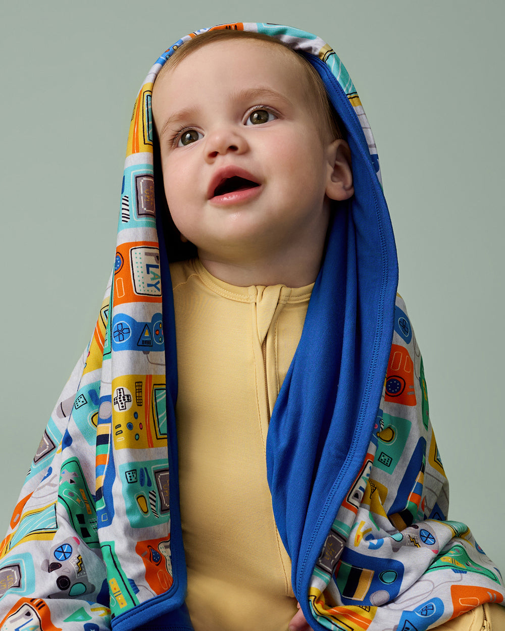 Close up of baby wearing a yellow zippy draped in the Game On Large Cloud Blanket®