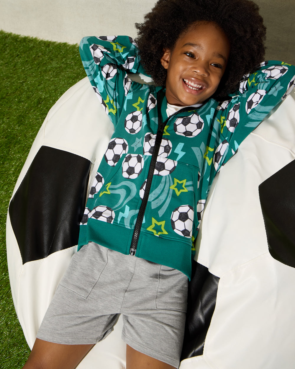 Boy wearing the Soccer Stars Zip Hoodie sitting on a soccer ball bean bag