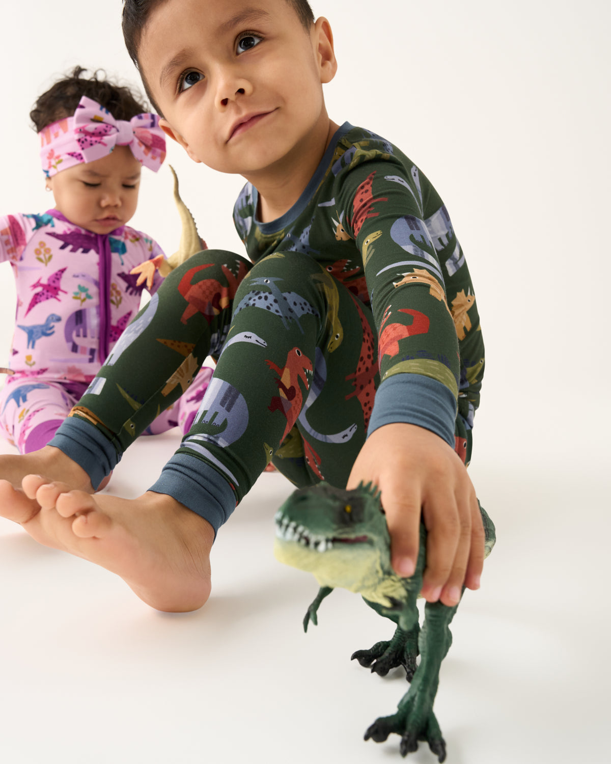 Child playing with a dinosaur toy wearing the Green Roar & Explore Two-Piece Pajama Set
