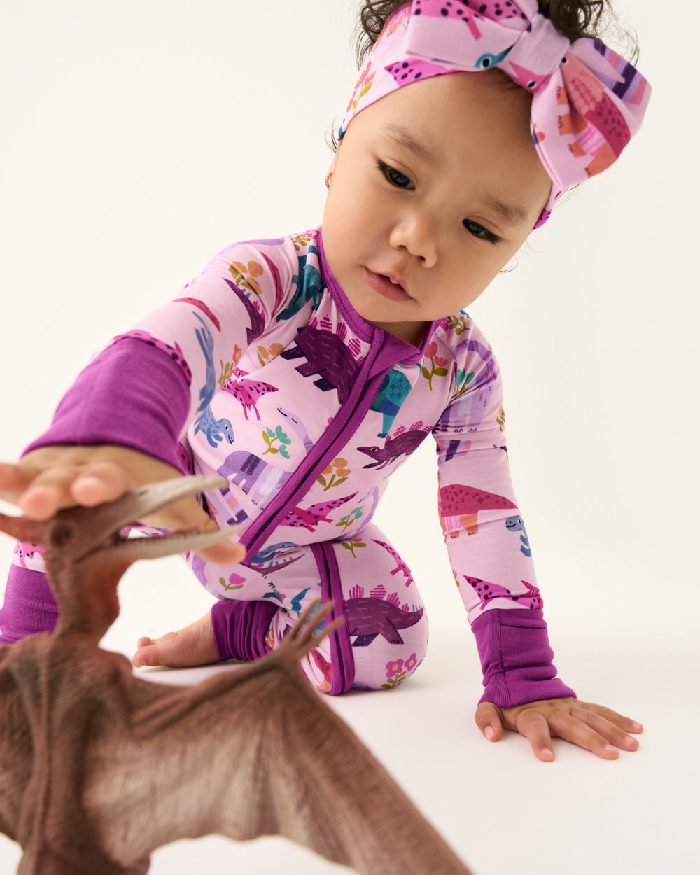 Crawling baby wearing the Pink Roar & Explore Zippy reaching for a dino figurine 