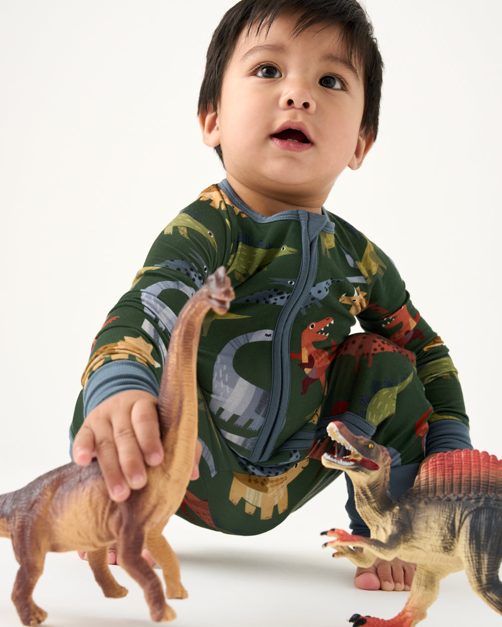 Baby playing with dinosaur figurines wearing the Green Roar & Explore Zippy