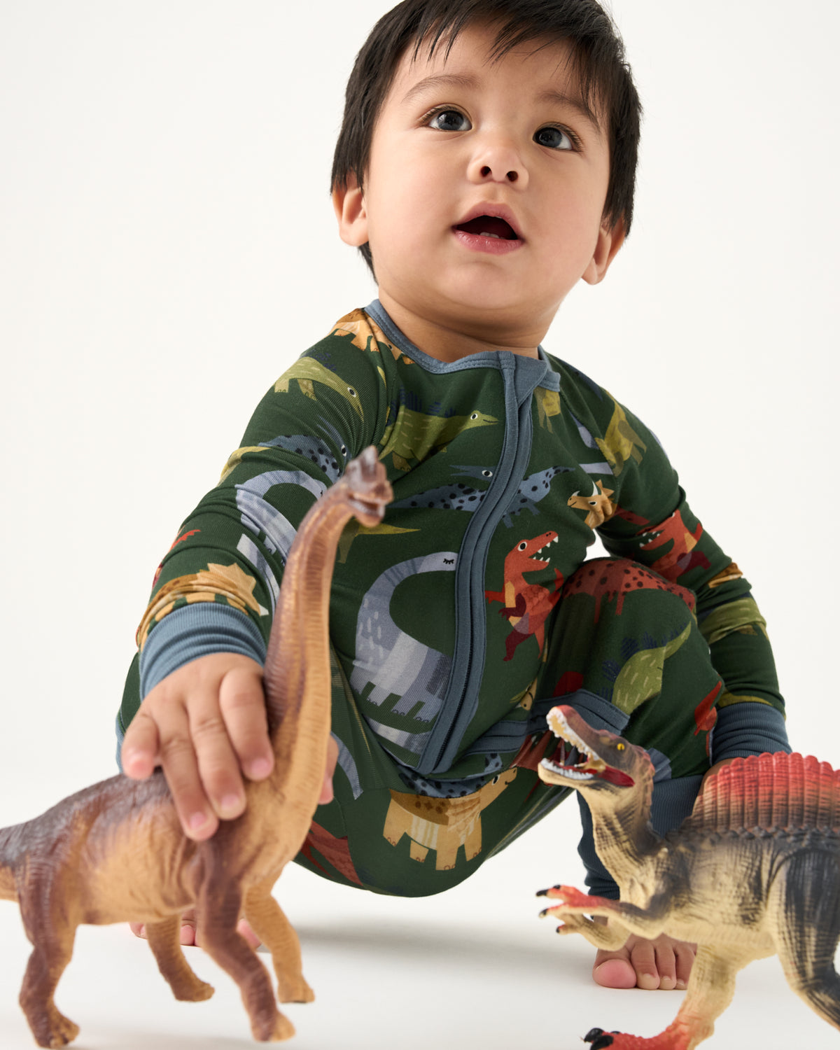 Baby playing with dinosaur figurines wearing the Green Roar & Explore Zippy
