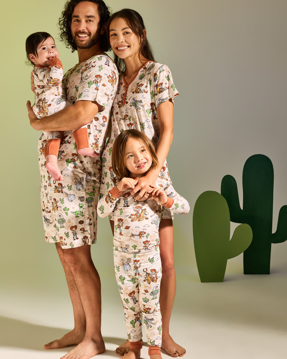 Family of four wearing matching Disney & Pixar Woody's Wild West pajamas on a green backdrop 