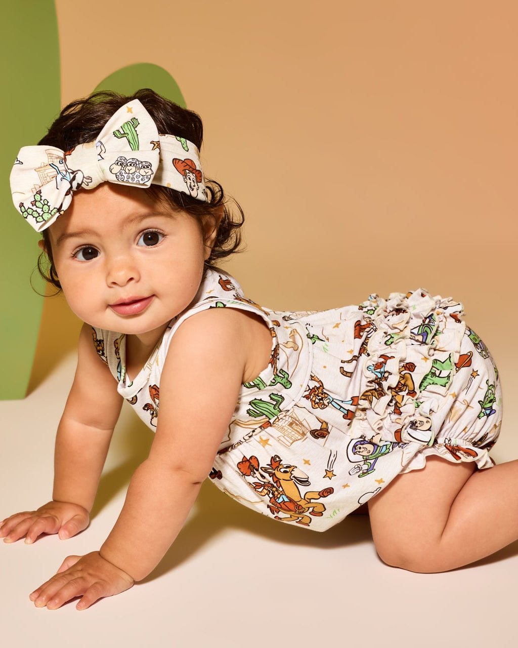 Crawling baby wearing the Disney & Pixar Woody's Wild West Bubble Romper and Luxe Bow