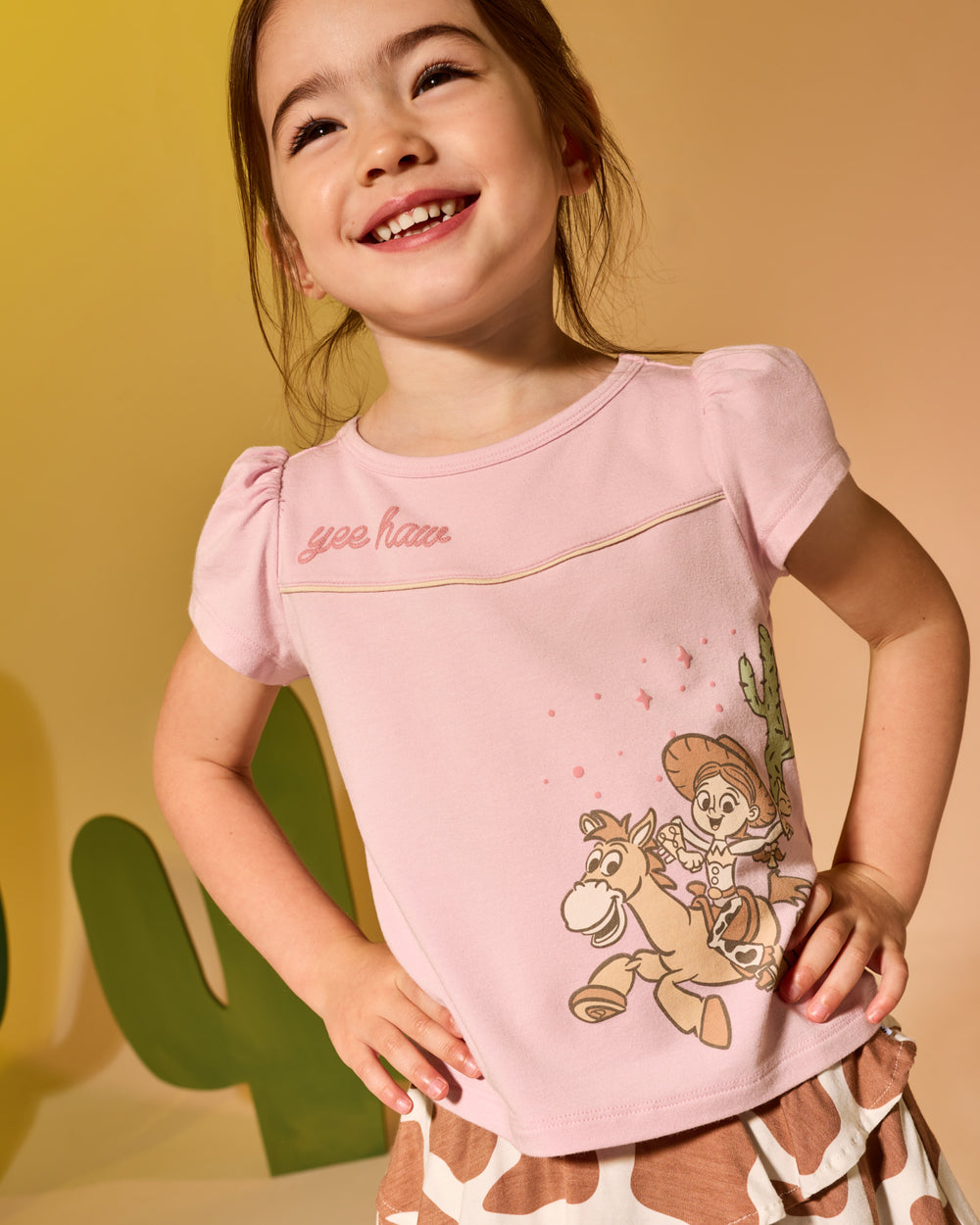 Girl wearing the Disney & Pixar Howdy Jessie Puff Sleeve Tee on a tan backdrop