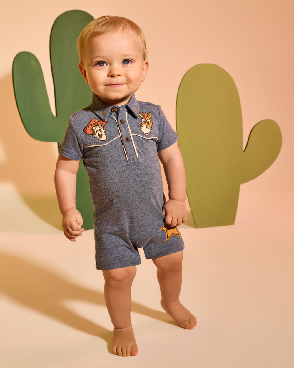 Baby wearing the Disney & Pixar The Roundup Gang Polo Shorty Romper with a cactus backdrop