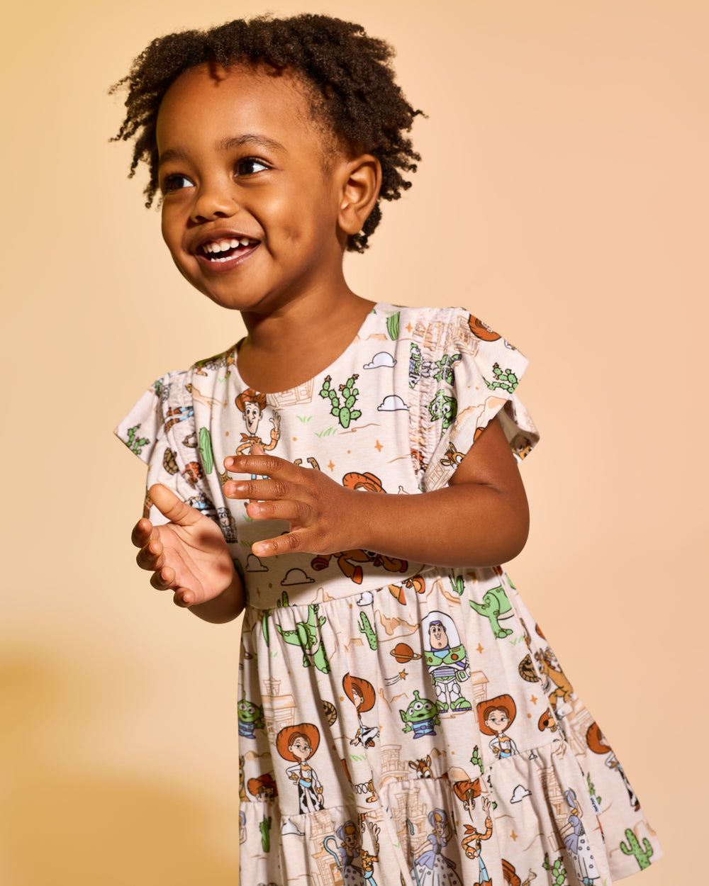 Girl wearing the Disney & Pixar Woody's Wild West Tiered Flutter Dress with Bloomer on a tan backdrop