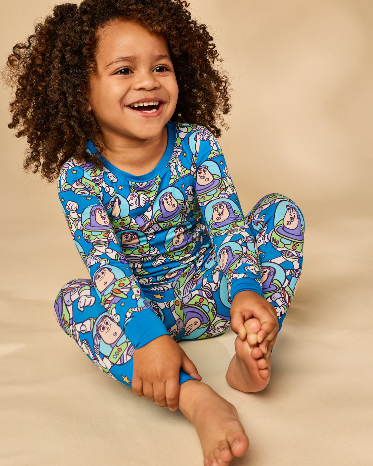 Sitting child wearing the Disney & Pixar Buzz's Cosmic Crew Two-Piece Pajama Set on a tan backdrop