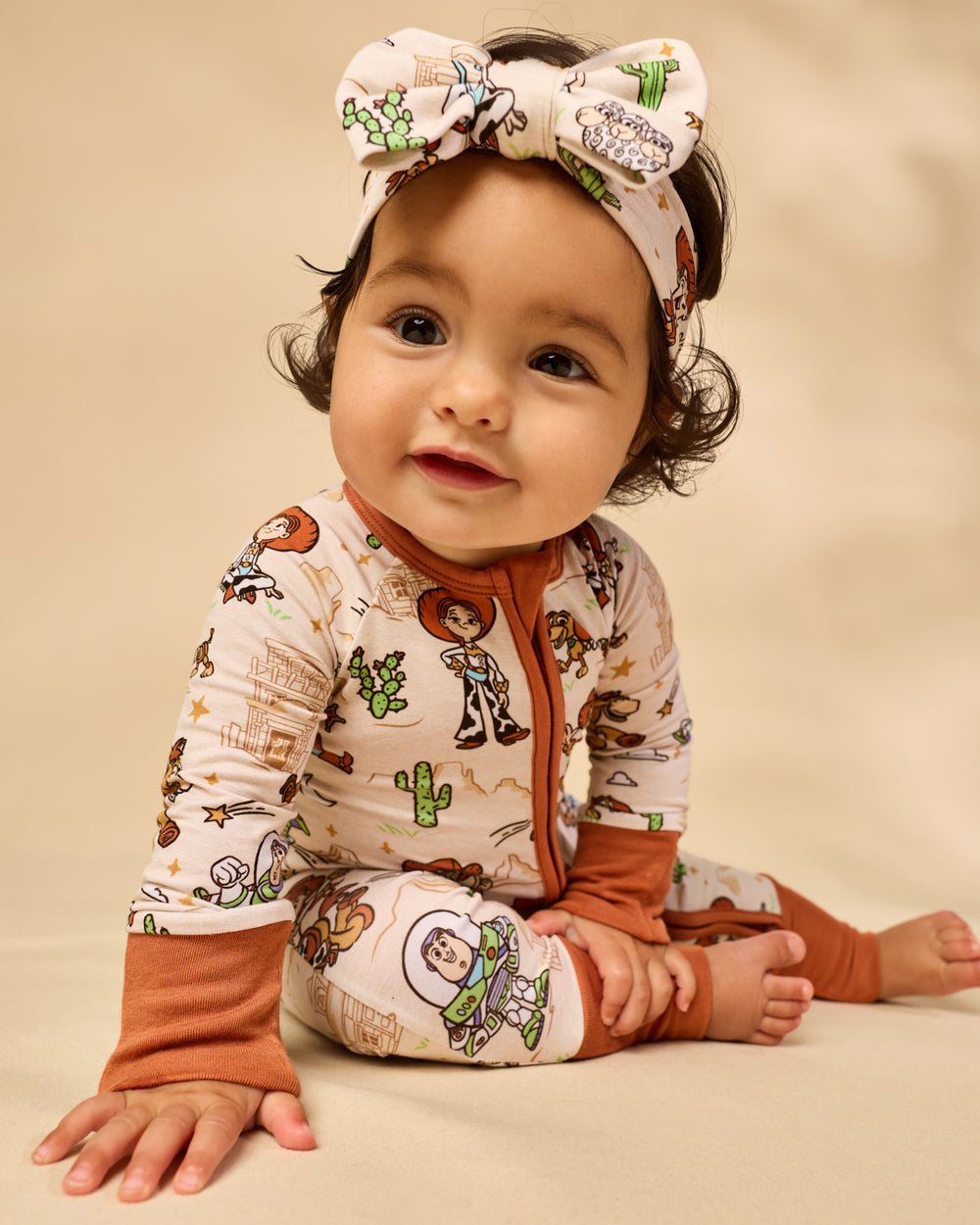 Baby wearing the Disney & Pixar Woody's Wild West Luxe Bow Headband and ZIppy on a tan backdrop