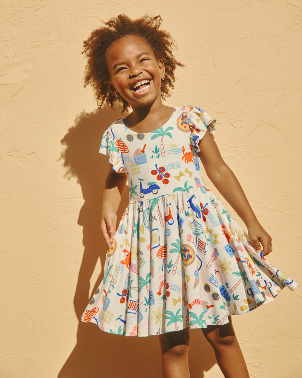 Girl wearing the Ciao Bella Flutter Twirl Dress on a yellow backdrop
