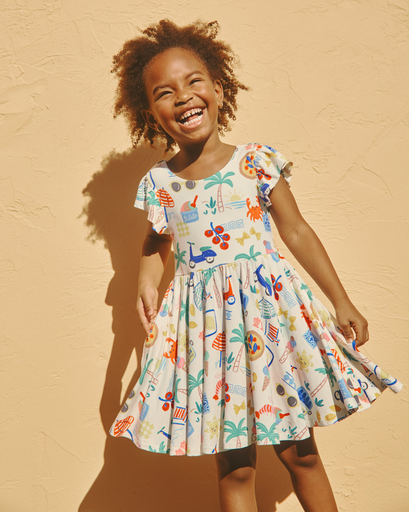 Girl wearing the Ciao Bella Flutter Twirl Dress on a yellow backdrop