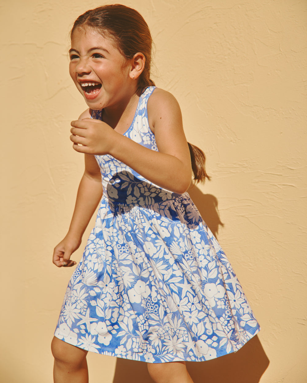 Girl wearing the Azure Garden Cross Back Skater Dress on a yellow backdrop