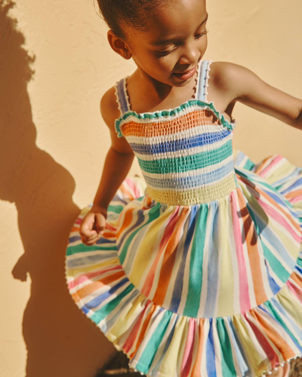 Twirling girl wearing the Rainbow Ribbon Smocked Tank Dress on a yellow backdrop