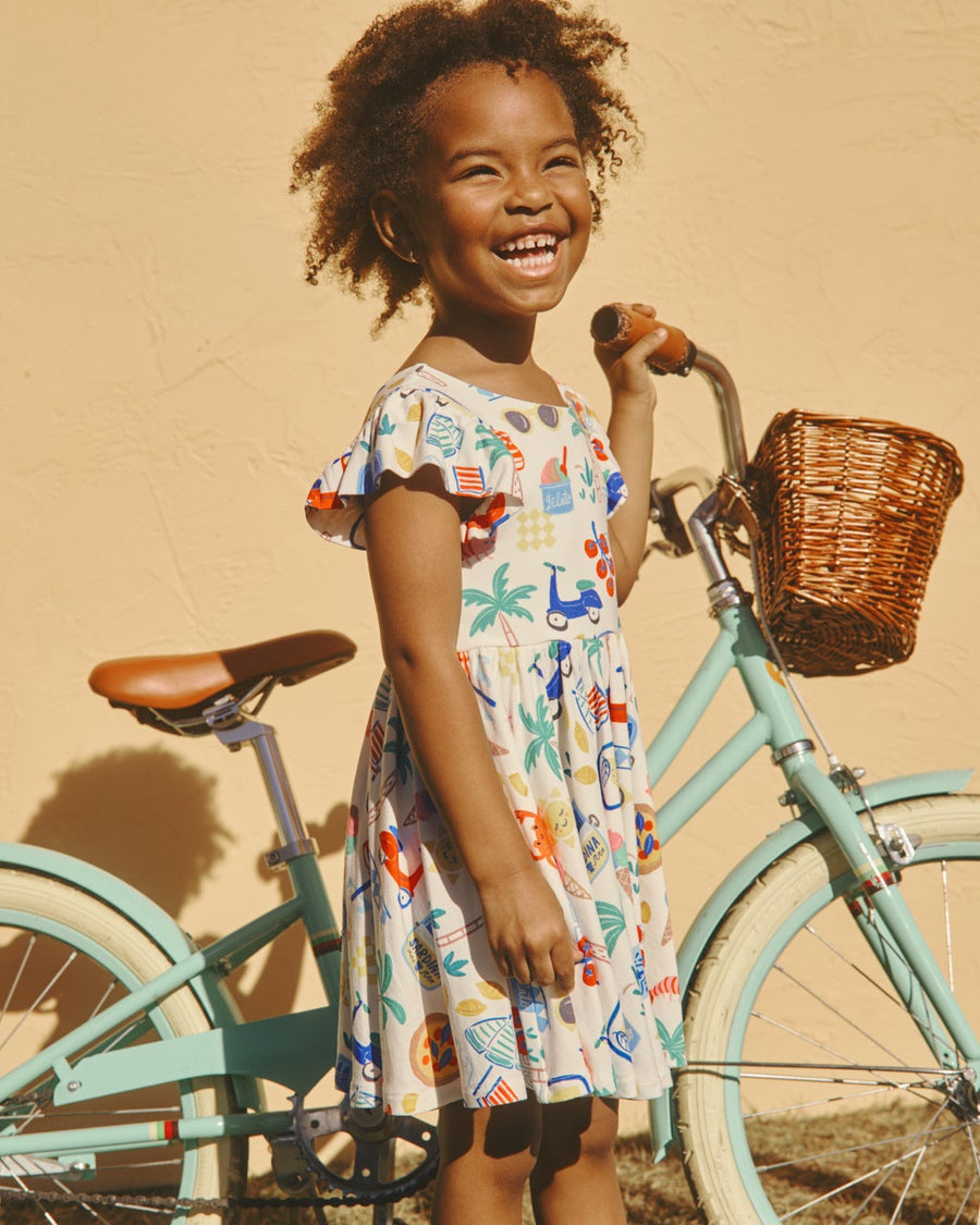 Girl holding onto a bike wearing the Ciao Bella Flutter Twirl Dress