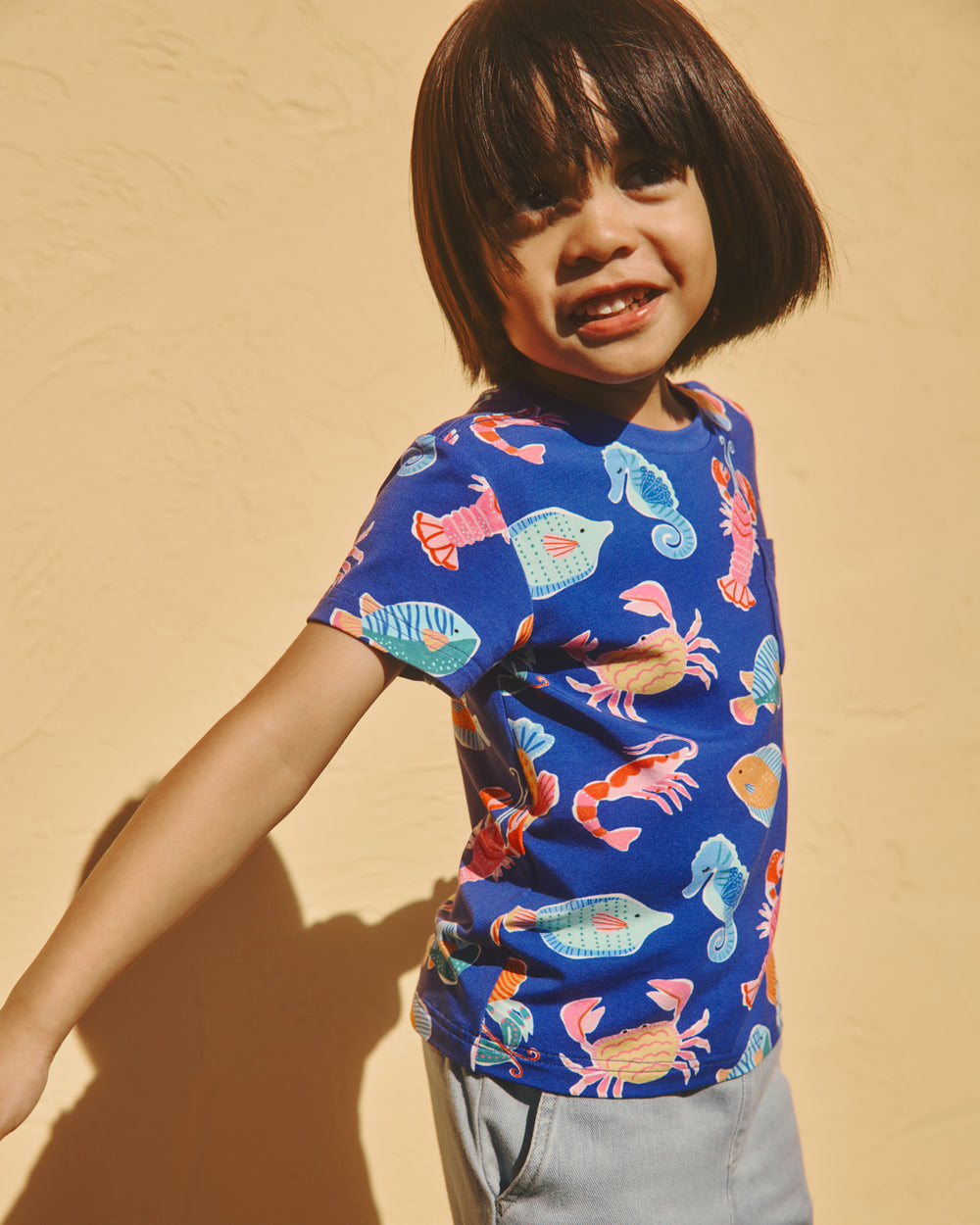 Child wearing the Tidepool Party Relaxed Pocket Tee on a yellow backdrop 