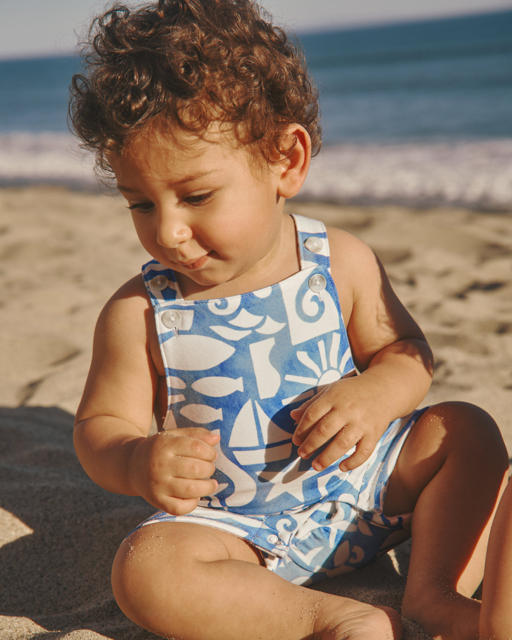 Baby at the beach wearing the Summer Shores Shorty Overall