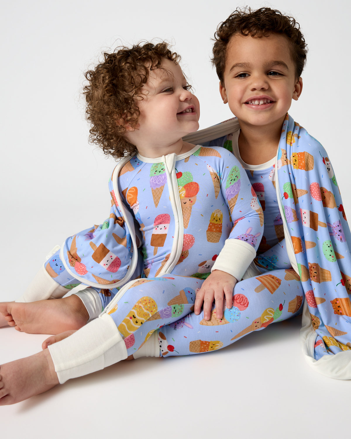 Two children wearing Scoop Squad PJs wrapped in a matching blanket