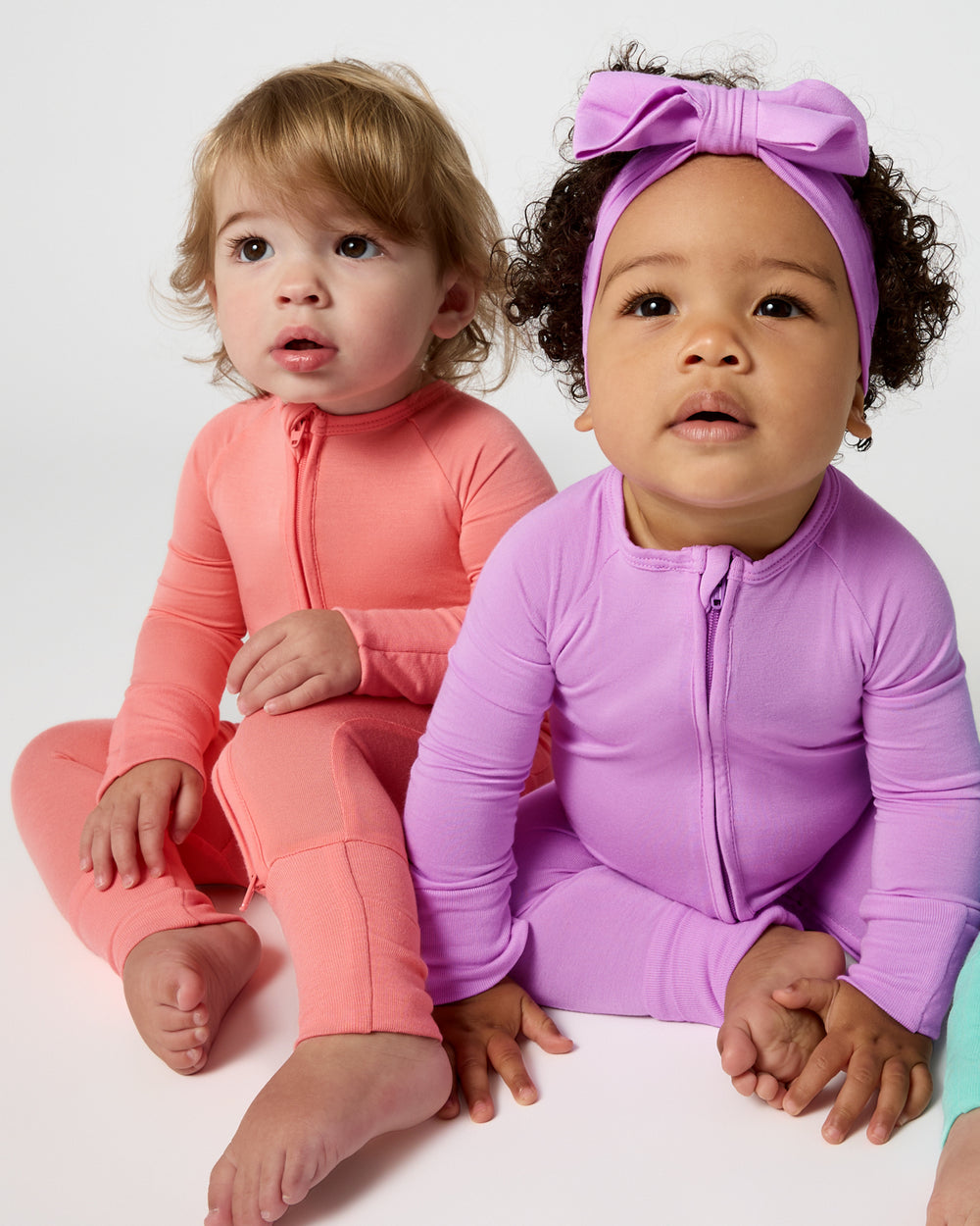 Two babies wearing Sweet Papaya and Soft Wisteria Zippies
