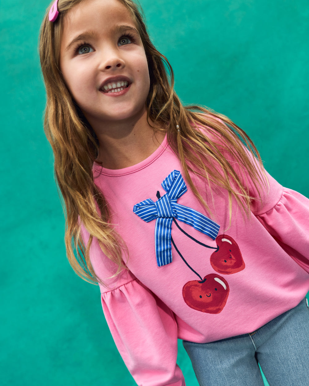 Girl wearing the Cherry Charm Drop Shoulder Crewneck on a teal back drop