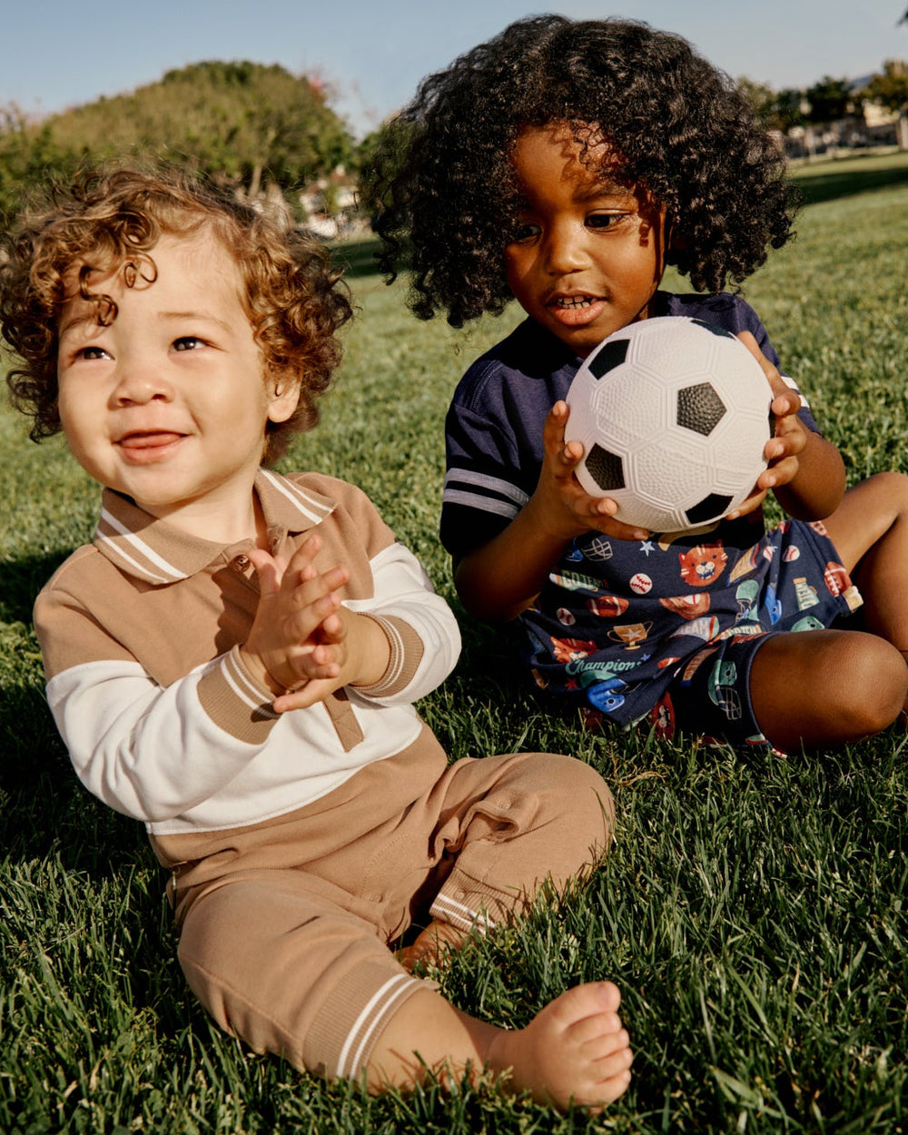 Two boys sitting in the grass wearing Varsity Themed daywear styles