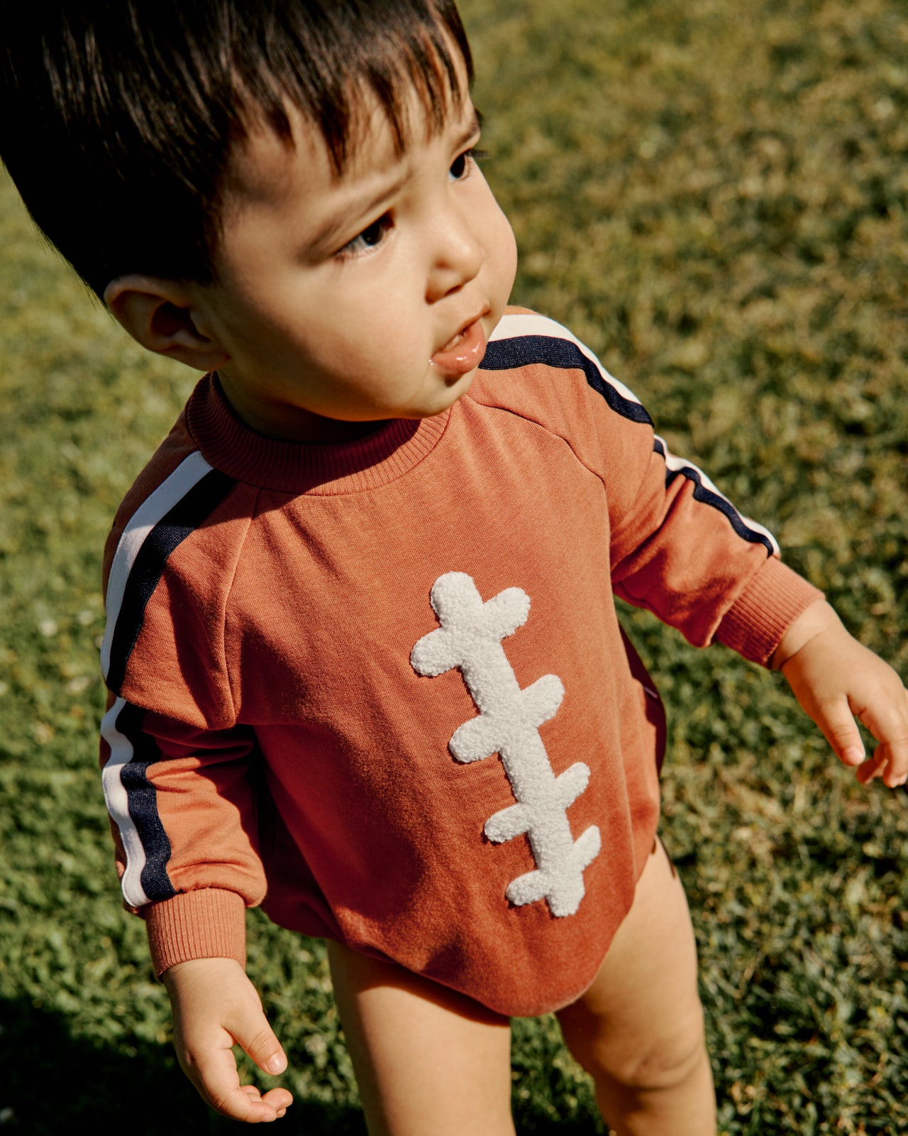 Boy wearing the Football Raglan Romper on a grassy field