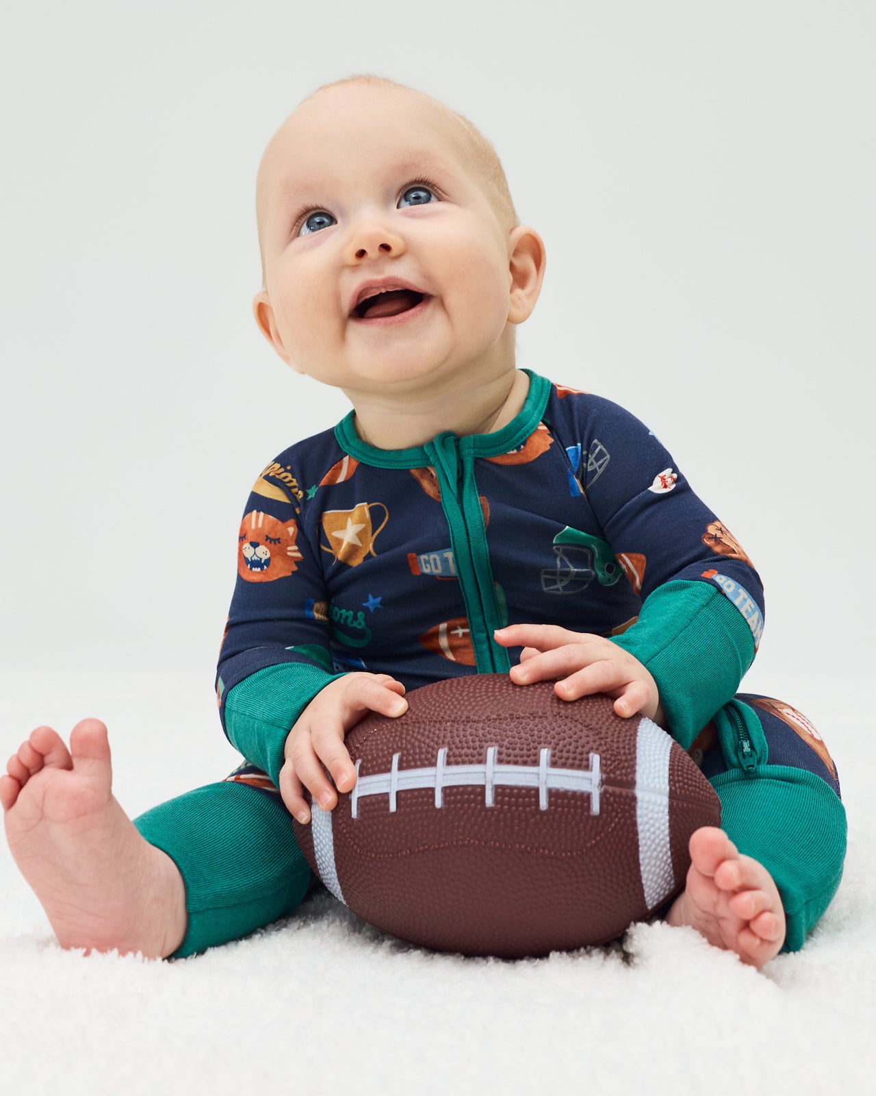 Sitting newborn wearing the Team Spirit Zippy holding a football