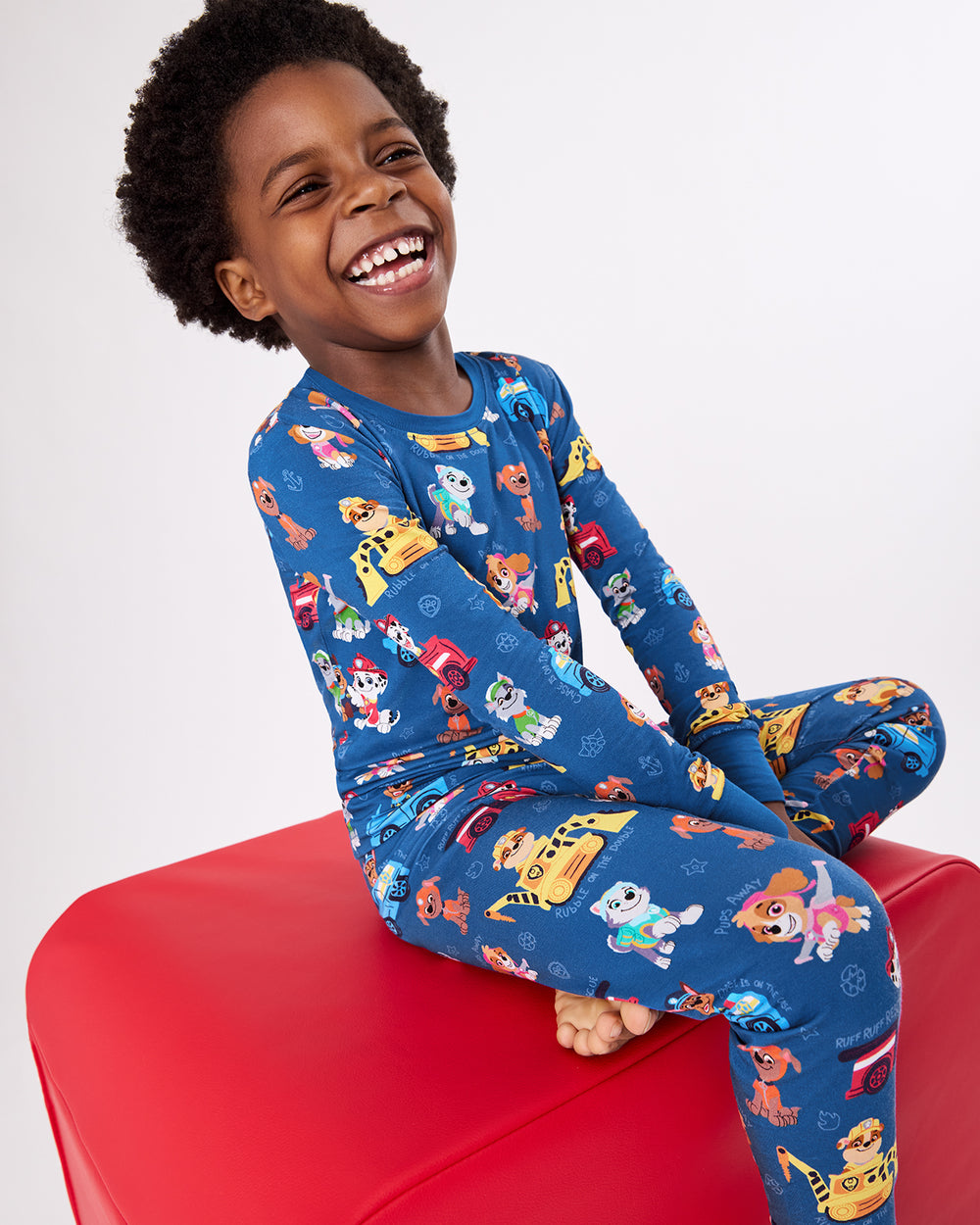 Boy sitting on a red ottoman wearing the PAW Patrol Adventure Bay Heroes Two-Piece Pajama Set