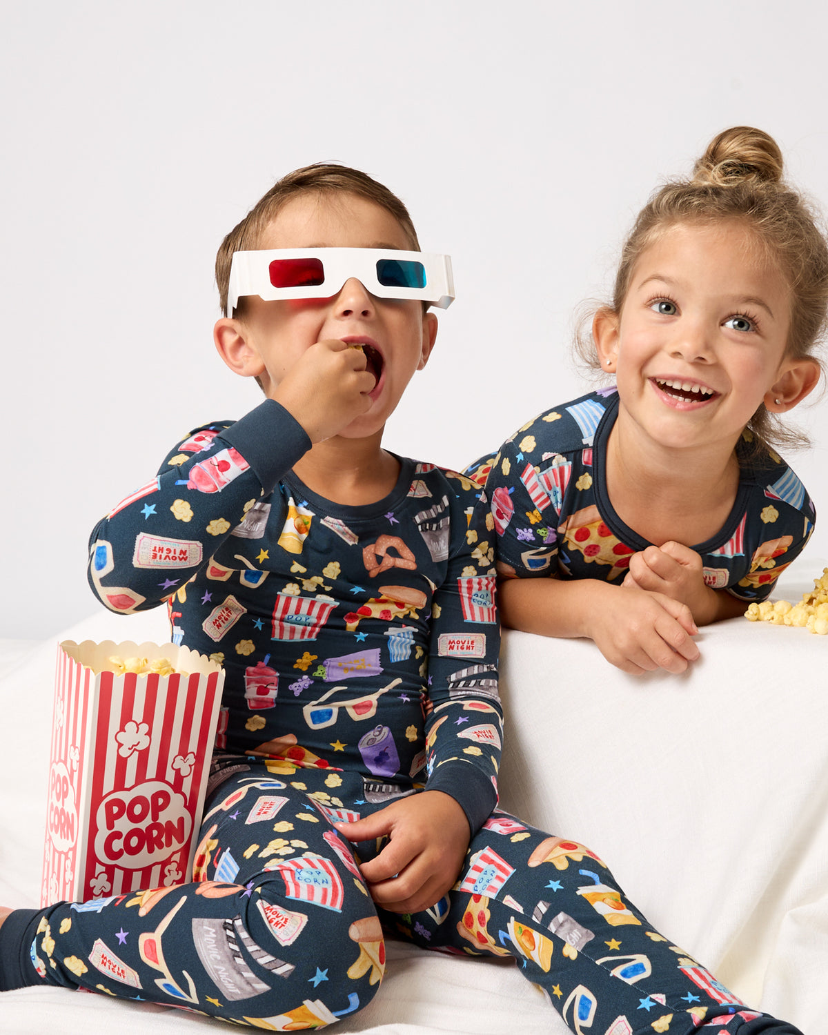 Two children wearing Movie Marathon Two-Piece Pajama Sets eating popcorn