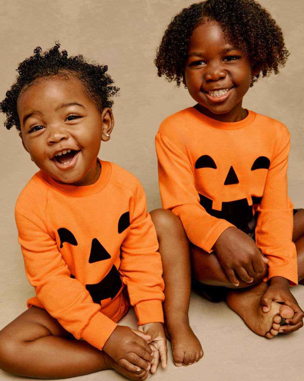 Two sitting children wearing matching Jack-O'-Lantern Halloween styles