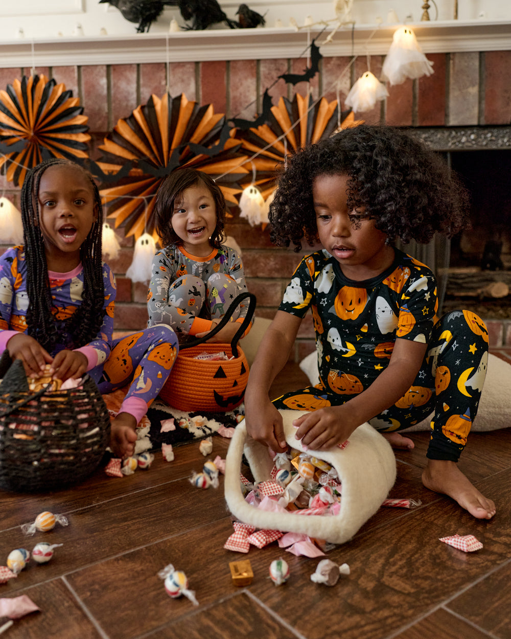 Three children wearing Halloween PJs trading candy