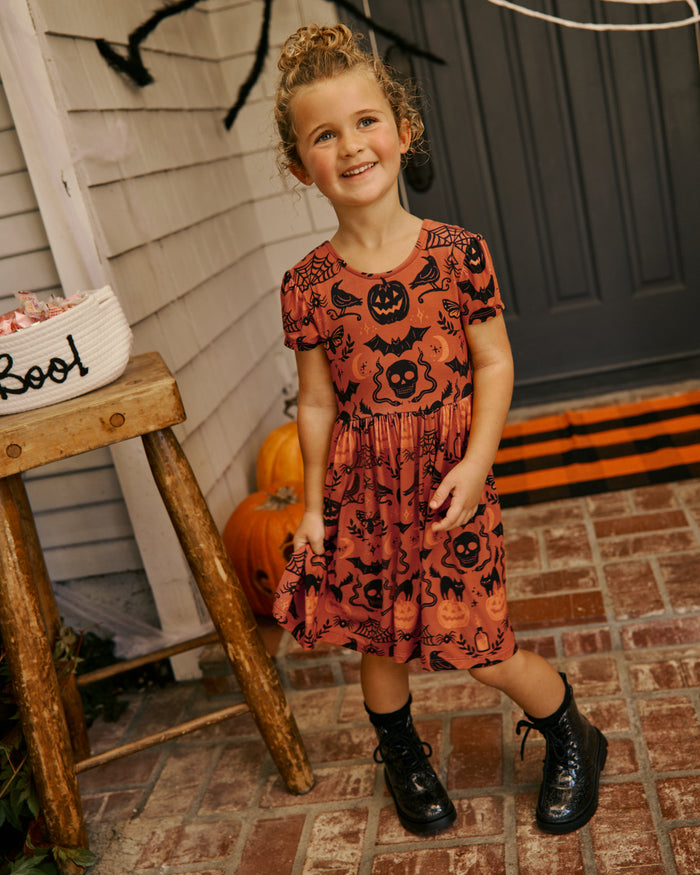 Girl wearing the Midnight Mischief Bow Back Skater Dress on a decorated front stoop