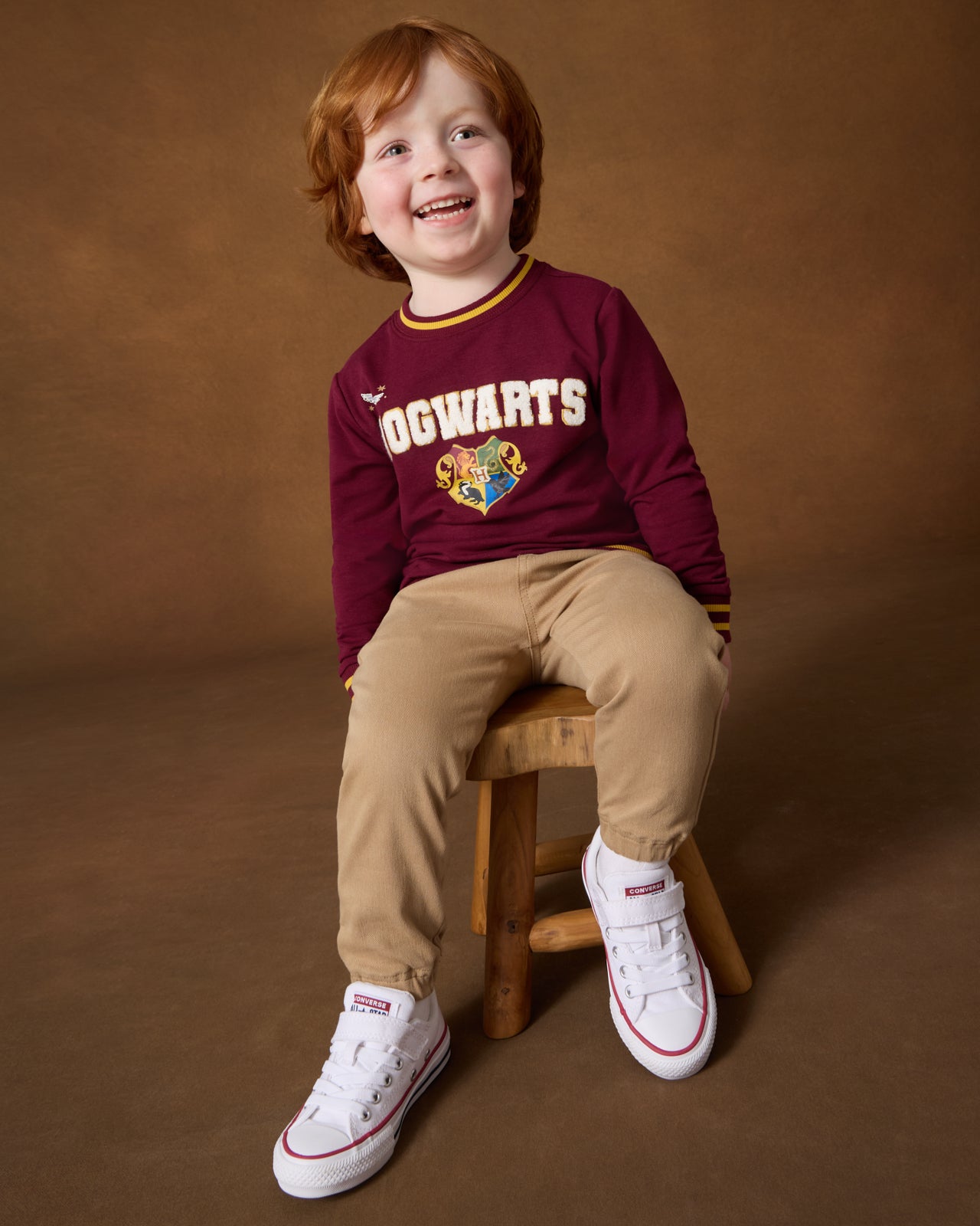 Boy wearing the Harry Potter™ Spellbinding Studies Crewneck Sweatshirt with khaki joggers sitting on a wooden stool