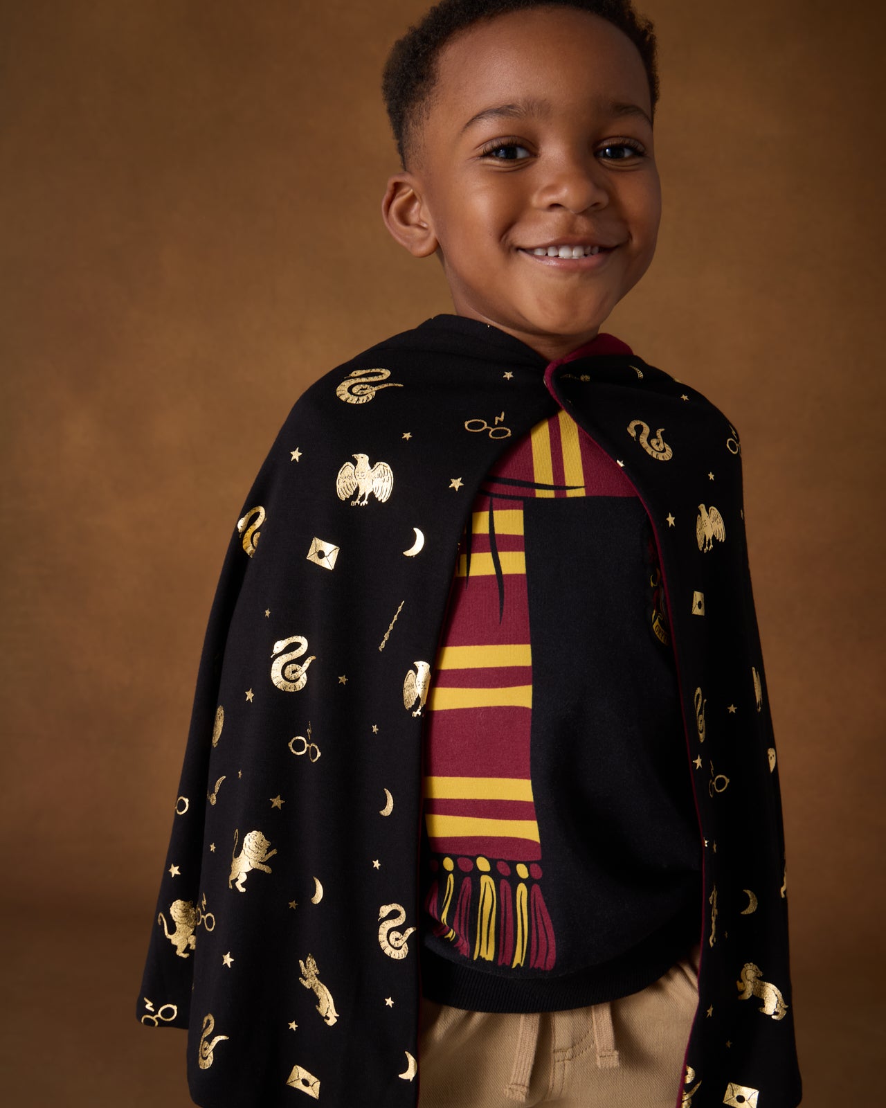 Boy wearing the Harry Potter™ Spellbinding Studies Hooded Cloak over the Gryffindor sweatshirt