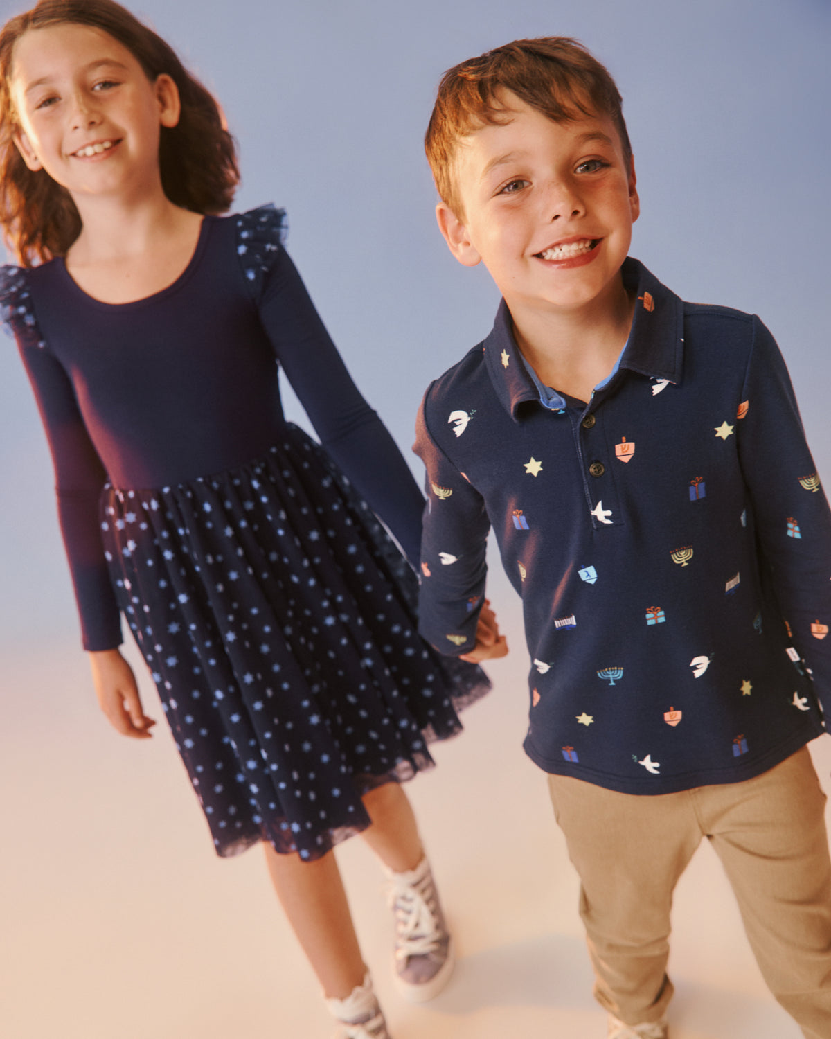 Two children wearing matching Hanukkah daywear styles on a soft blue backdrop 